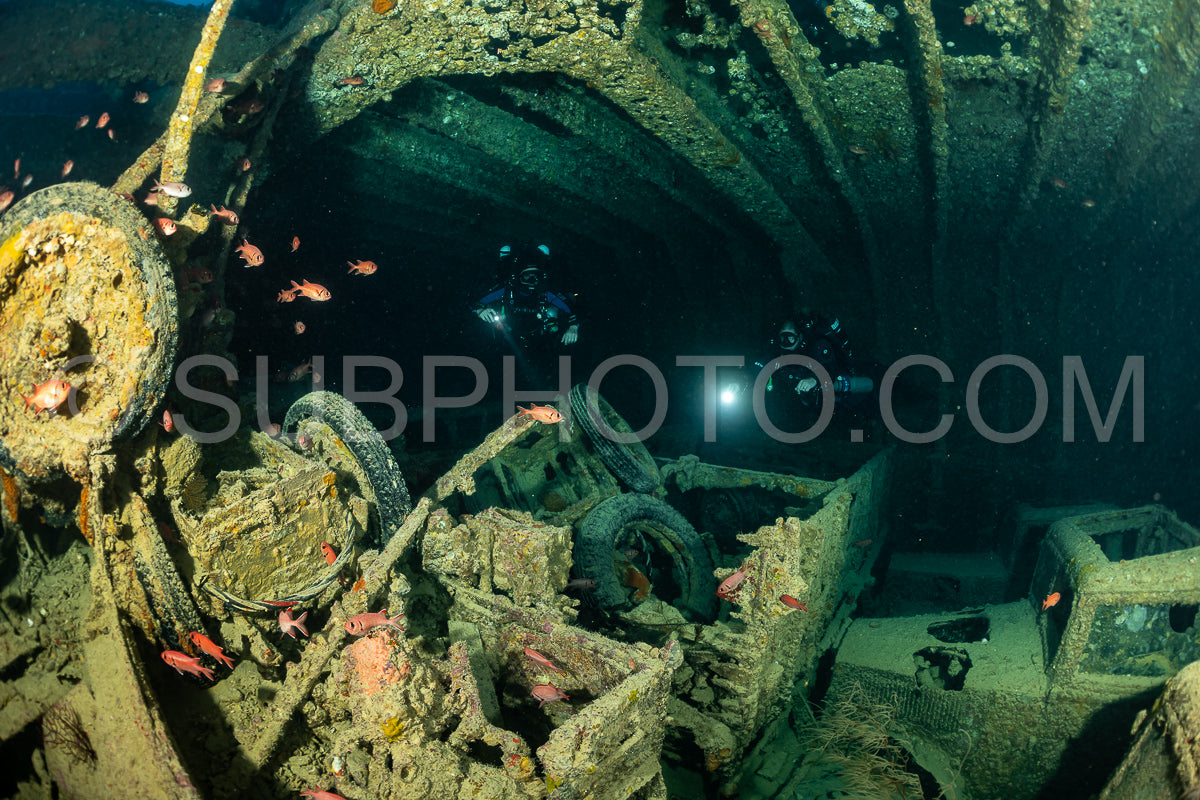 Two divers- using rebreathers- explore the interior of a large- sunken ship in the Red Sea. They are illuminated by their headlamps.