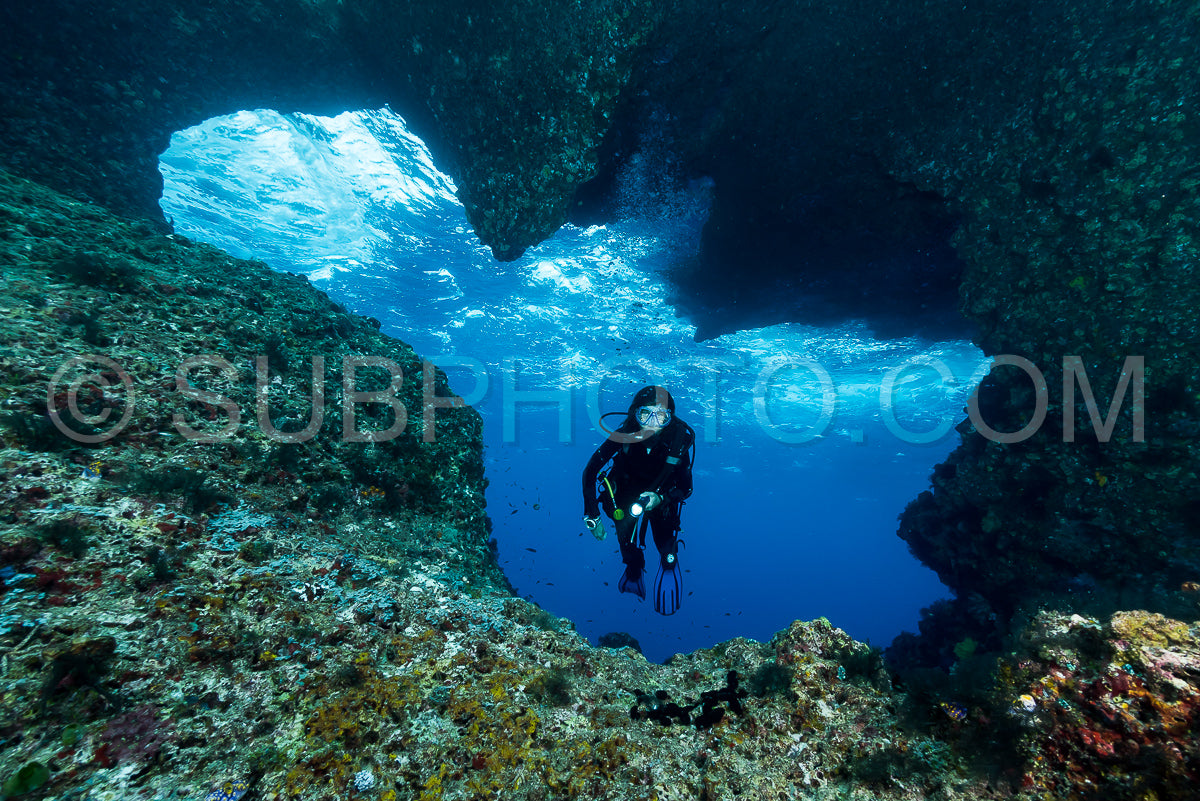 woman diver underwater at the entrance of a cave with sunrays
