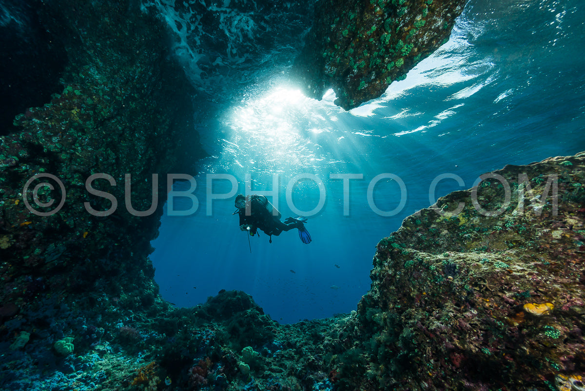 woman diver underwater at the entrance of a cave with sunrays