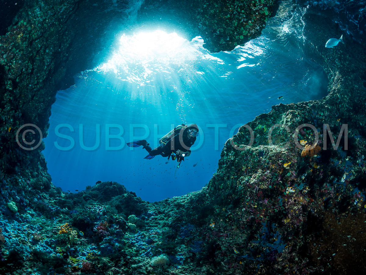 woman diver underwater at the entrance of a cave with sunrays