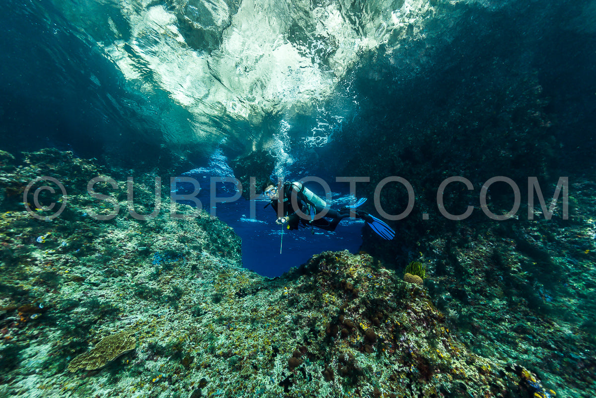 woman diver underwater at the entrance of a cave with sunrays