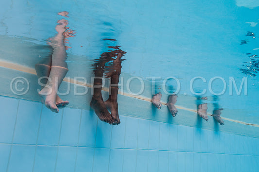 Feet of four women underwater in a pool