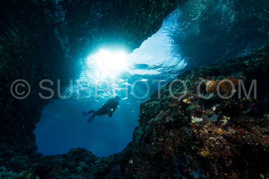 woman diver underwater at the entrance of a cave with sunrays
