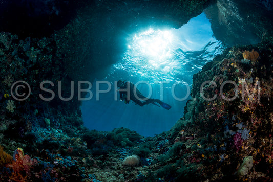 woman diver underwater at the entrance of a cave with sunrays
