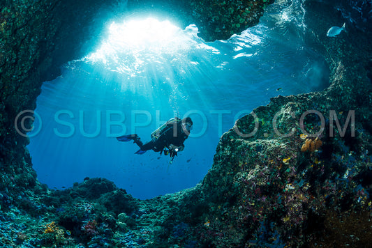 Photo de femme plongeant sous l'eau à l'entrée d'une grotte avec des rayons de soleil