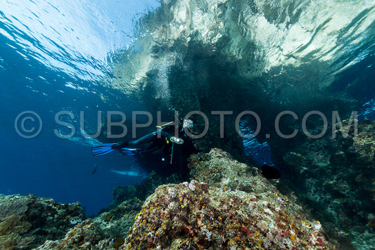 woman diver underwater at the entrance of a cave with sunrays
