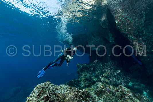 woman diver underwater at the entrance of a cave with sunrays