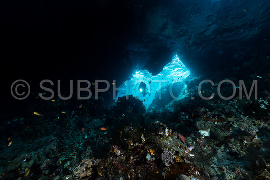 woman diver underwater at the entrance of a cave with sunrays