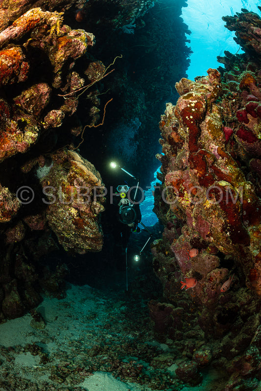 typical underwater cave in a red sea reef with an underwater photographer diver