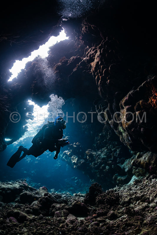 typical underwater cave in a red sea reef with an underwater photographer diver