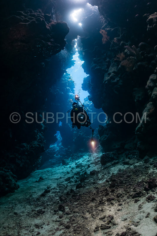 typical underwater cave in a red sea reef with an underwater photographer diver