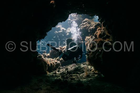 typical underwater cave in a red sea reef with an underwater photographer diver
