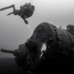 Black and white: diver with torch above encrusted wreck machinery, Ville de Rochefort wreck, Brittany, France