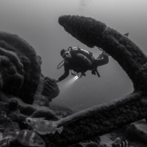 Black and white: diver framed by a large encrusted anchor on the wreck, Ville de Rochefort wreck, Brittany, France