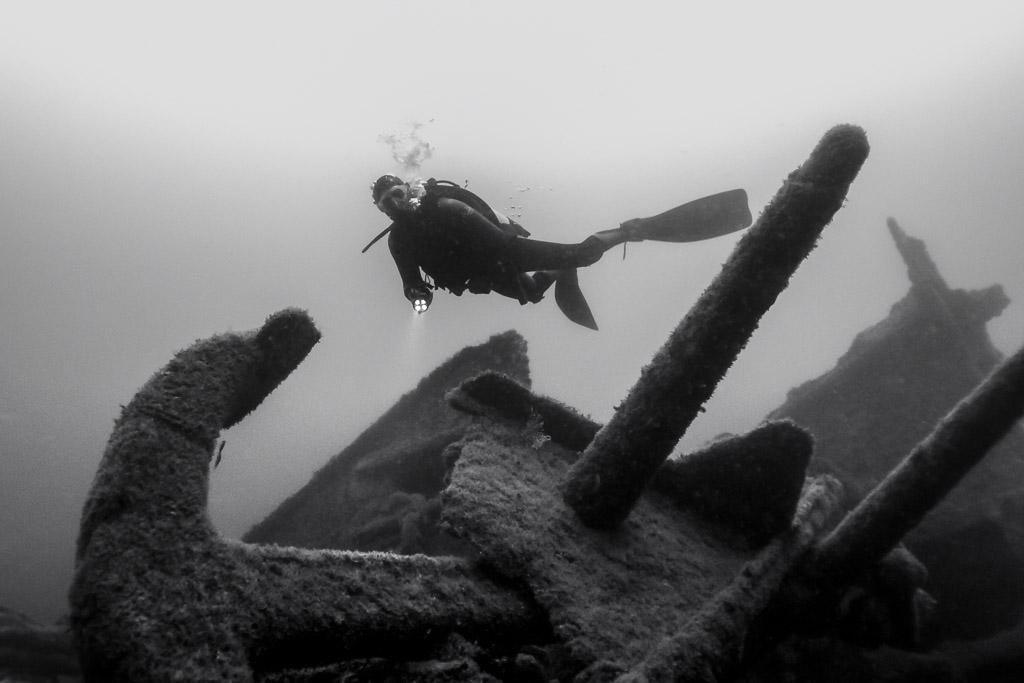 Black and white: diver above an anchor and scattered wreck debris, Ville de Rochefort wreck, Brittany, France