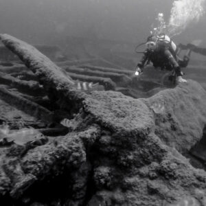 Black and white: diver with torch inspecting the wreck bow with fish, Ville de Rochefort wreck, Brittany, France