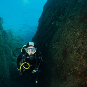 Woman diver rising through a narrow rocky canyon, vertical, Porto-Vecchio, Corsica, France