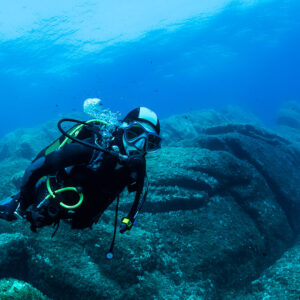 Woman diver swimming horizontally over sculpted rock ridges, Porto-Vecchio, Corsica, France
