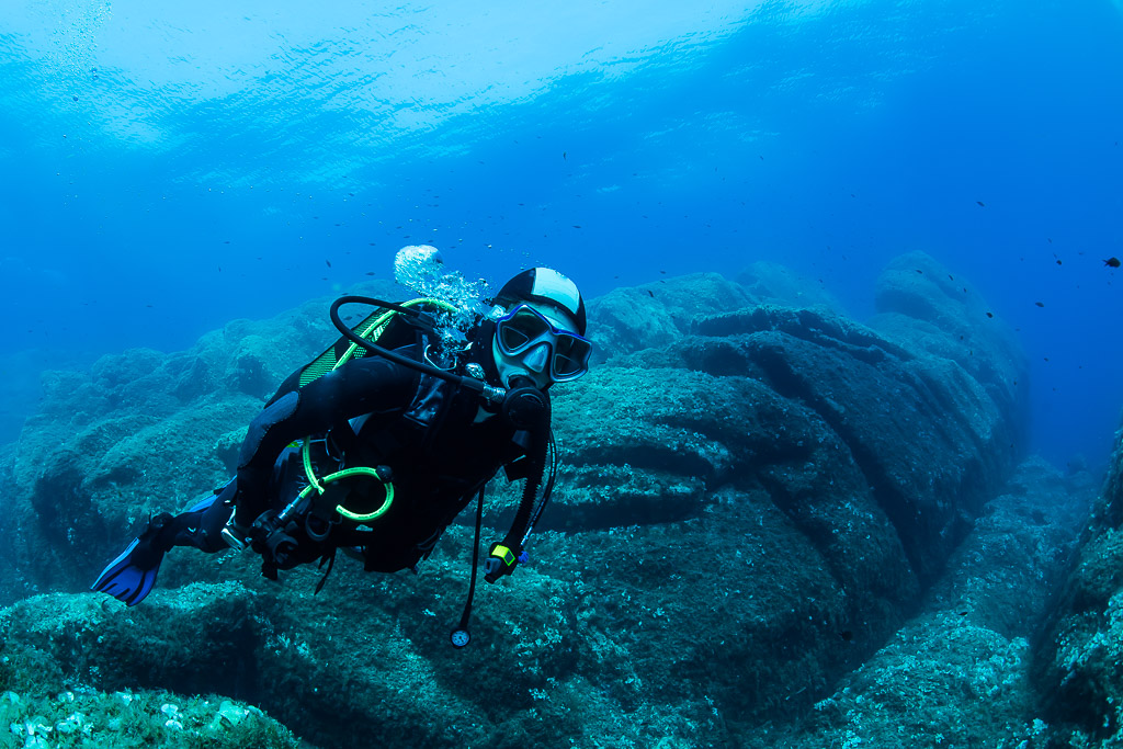 Woman diver swimming horizontally over sculpted rock ridges, Porto-Vecchio, Corsica, France