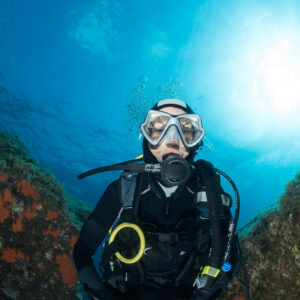 Woman diver waist-up portrait in a rocky gully, sun behind, Porto-Vecchio, Corsica, France