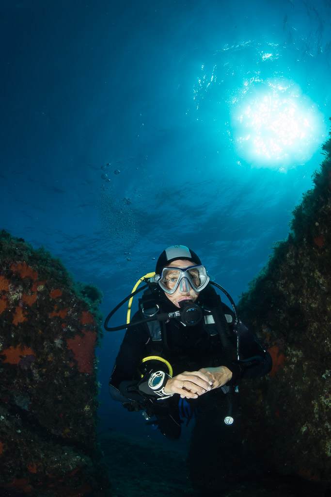 Woman diver in a shadowed gully with sunburst upper right, Porto-Vecchio, Corsica, France
