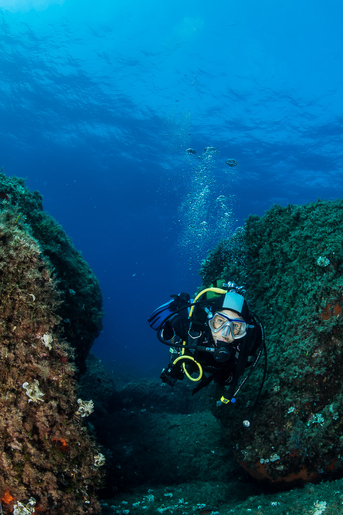 Woman diver peering out between two large rocks, Porto-Vecchio, Corsica, France