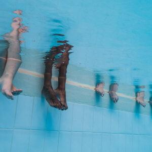 Legs and feet of four people dangling into a swimming pool