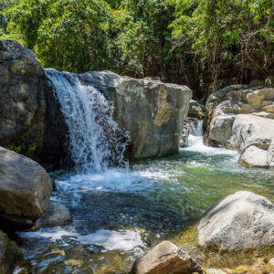 Small waterfall pouring between large boulders into a clear pool, Puerto Galera, Mindoro, Philippines