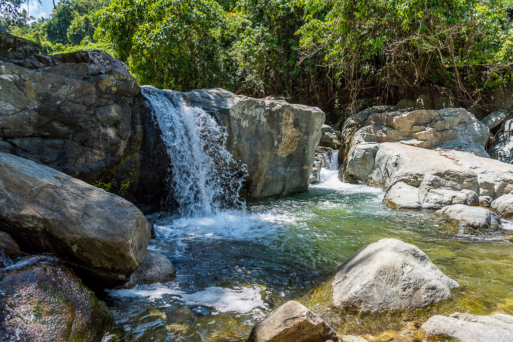 Small waterfall pouring between large boulders into a clear pool, Puerto Galera, Mindoro, Philippines