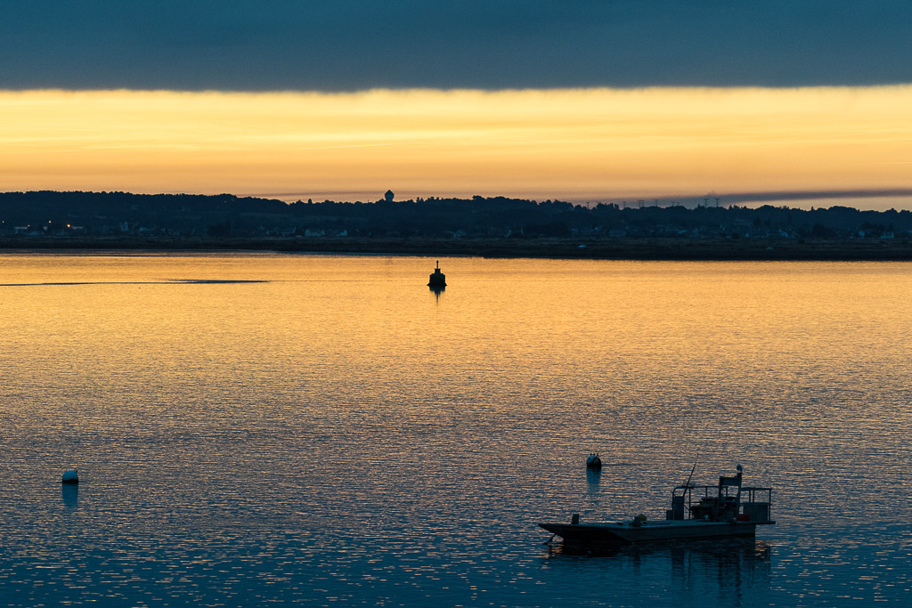 Golden dawn sky over calm bay with silhouetted work barge, Le Croisic, Brittany, France