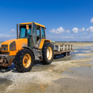 Tracteur orange en gros plan tirant une remorque dans l’eau peu profonde de l’estran, Le Croisic, Bretagne, France