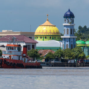 Red tugboat on a river in front of a golden-domed mosque and blue minaret, Maratua, Kalimantan (Borneo), Indonesia