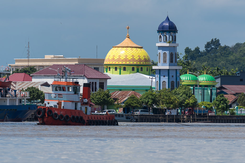 Red tugboat on a river in front of a golden-domed mosque and blue minaret, Maratua, Kalimantan (Borneo), Indonesia