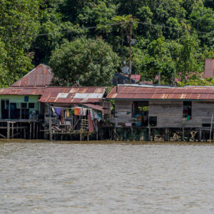 Wooden stilt houses with rusty tin roofs on a jungle riverbank, Maratua, Kalimantan (Borneo), Indonesia