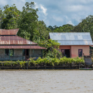 Riverside house with tiered red roof beside a pink house among trees, Maratua, Kalimantan (Borneo), Indonesia