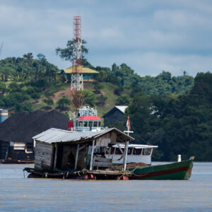 Small houseboat and green wooden boat before a coal stockpile and telecom mast, Maratua, Kalimantan (Borneo), Indonesia