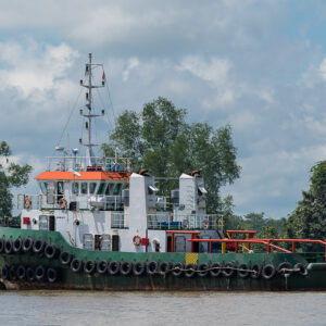 Green-hulled tugboat with tyre fenders sailing on the river, side view, Maratua, Kalimantan (Borneo), Indonesia