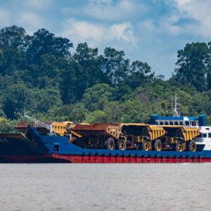 Barge chargée de tombereaux miniers jaunes naviguant devant la forêt tropicale, Maratua, Kalimantan (Bornéo), Indonésie