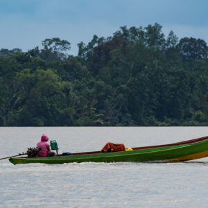 Boatman in a pink hood steering a green wooden longboat, Maratua, Kalimantan (Borneo), Indonesia