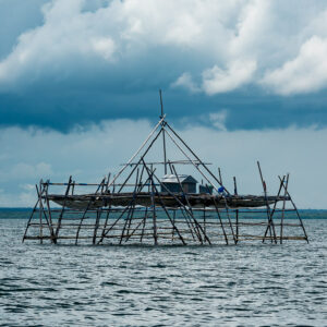 Bagang fishing platform under dark storm clouds over grey water, Maratua, Kalimantan (Borneo), Indonesia