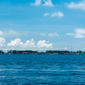 Low flat island with village on the horizon across deep blue sea, Maratua, Kalimantan (Borneo), Indonesia