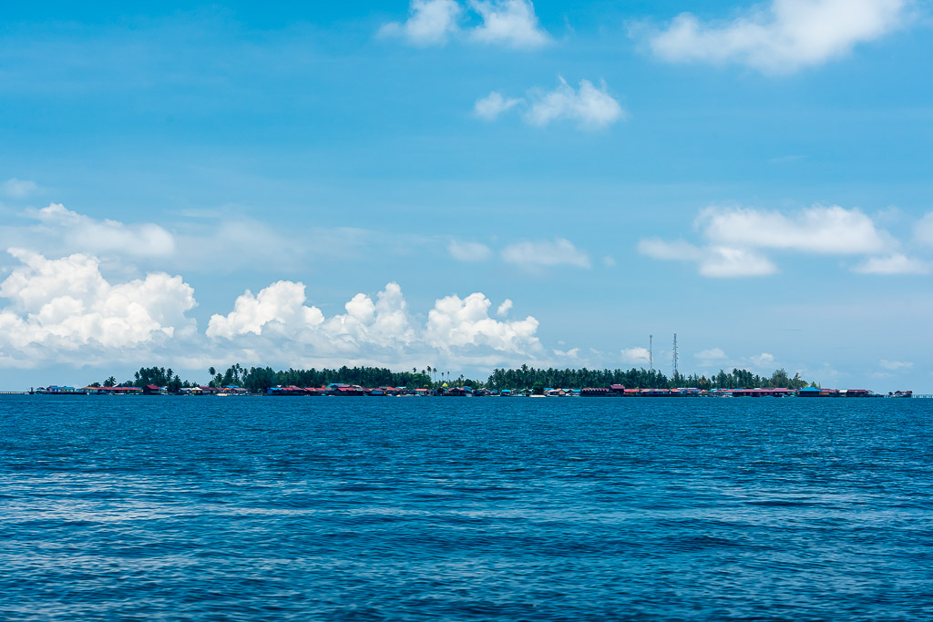 Low flat island with village on the horizon across deep blue sea, Maratua, Kalimantan (Borneo), Indonesia