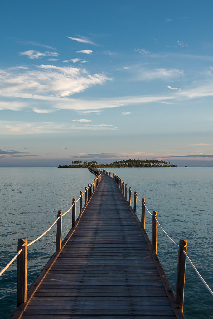 Wooden jetty leading to a distant island at dusk, vertical, Maratua, Kalimantan (Borneo), Indonesia