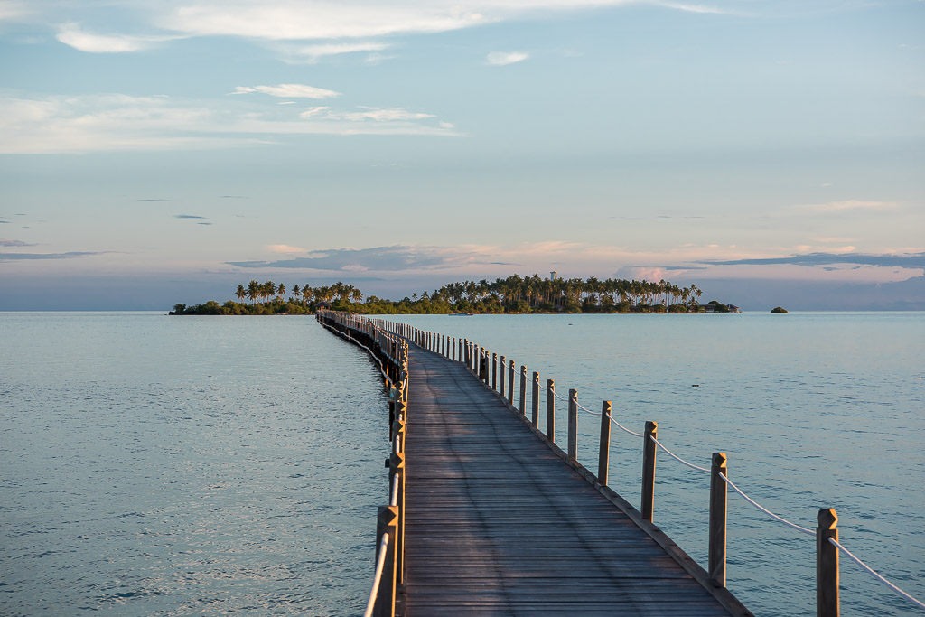 Long wooden jetty stretching towards a palm islet in soft evening light, Maratua, Kalimantan (Borneo), Indonesia