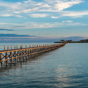 Person sitting on a long wooden pier over calm sea at dusk, Maratua, Kalimantan (Borneo), Indonesia