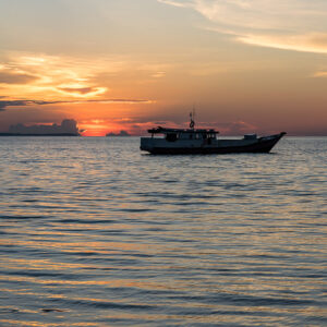 Silhouetted wooden boat on calm sea under orange sunset clouds, Maratua, Kalimantan (Borneo), Indonesia