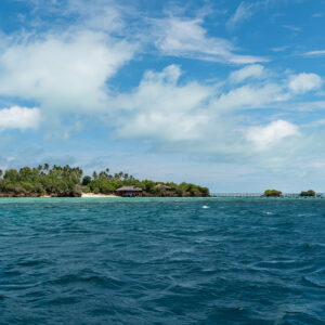 Low green island with long jetty seen across a deep blue sea, Maratua, Kalimantan (Borneo), Indonesia