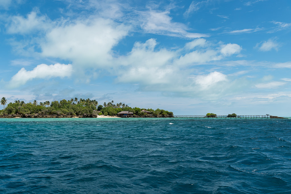 Low green island with long jetty seen across a deep blue sea, Maratua, Kalimantan (Borneo), Indonesia