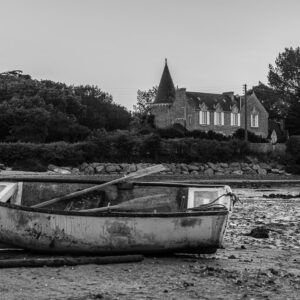 Black-and-white old rowing boat stranded on mudflat before turreted manor, Le Croisic, Brittany, France
