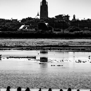 Black-and-white church tower above village reflected in tidal pools with posts, Le Croisic, Brittany, France
